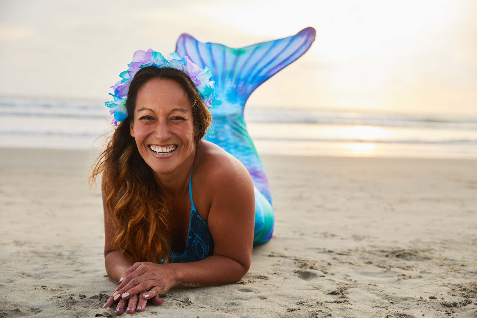 Mature woman in a mermaid costume laughing on a sandy beach